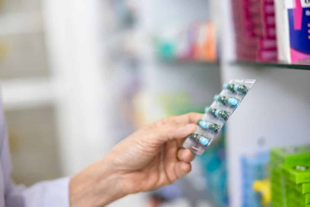 Hand holding blister pack of capsules in pharmacy.