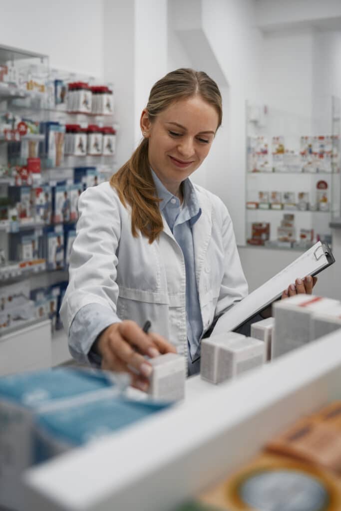 Pharmacist organizing medicine boxes on pharmacy shelf.