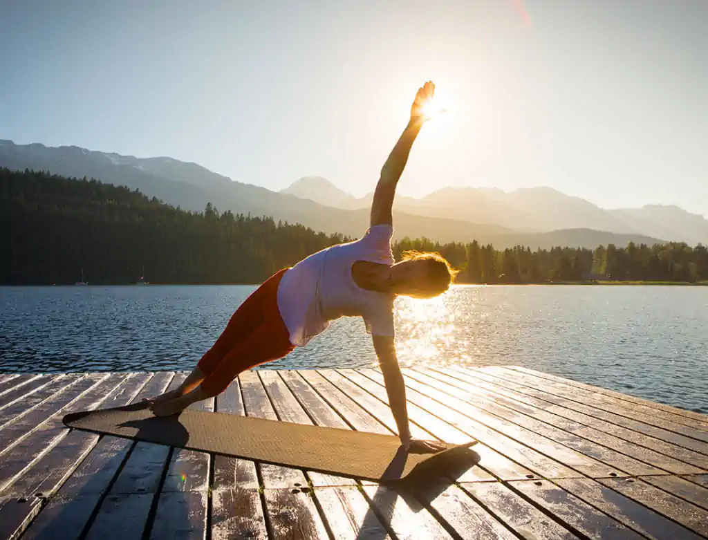 Person doing side plank yoga on lakeside dock